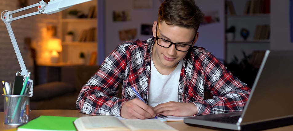 High school student sitting at desk with laptop writing his college essay