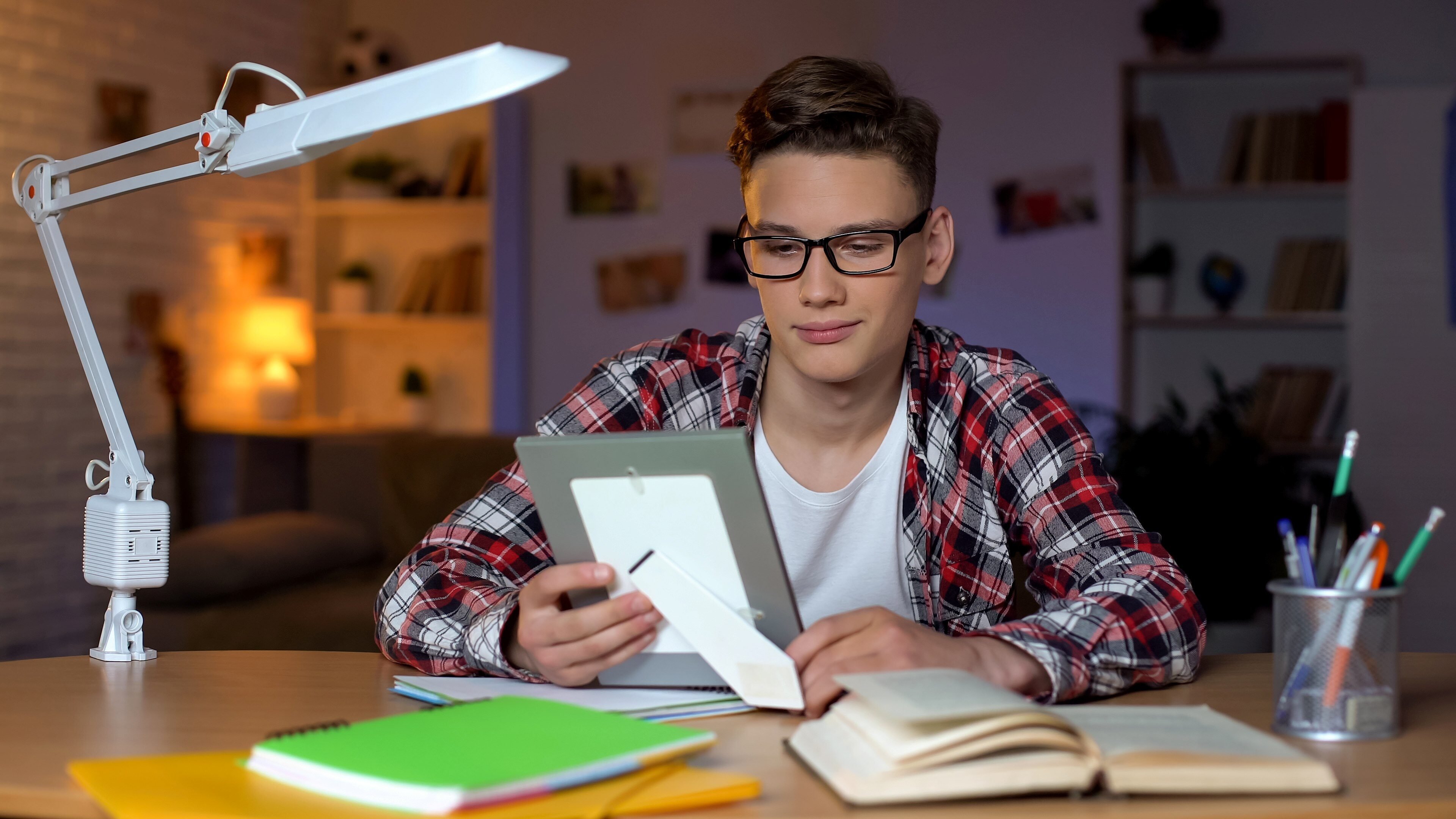 Young college student sitting on bed in dorm room talking to family on laptop
